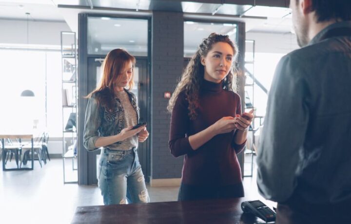 Three young adults engage at a cafe counter, using mobile devices.