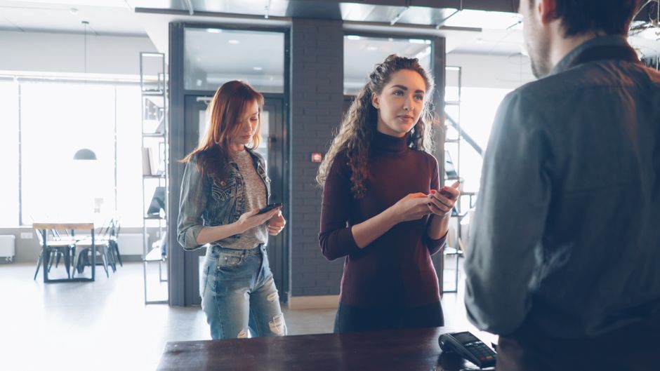 Three young adults engage at a cafe counter, using mobile devices.