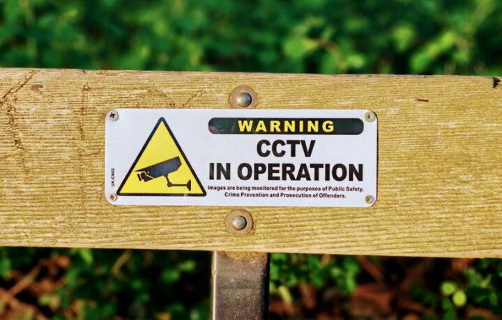 Wooden bench with a CCTV in operation warning sign, emphasizing public safety.