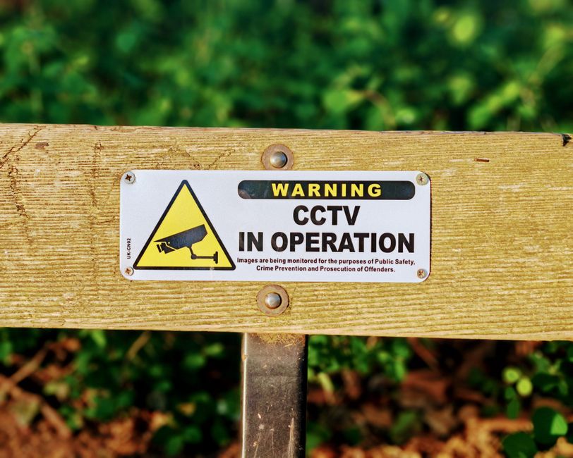 Wooden bench with a CCTV in operation warning sign, emphasizing public safety.