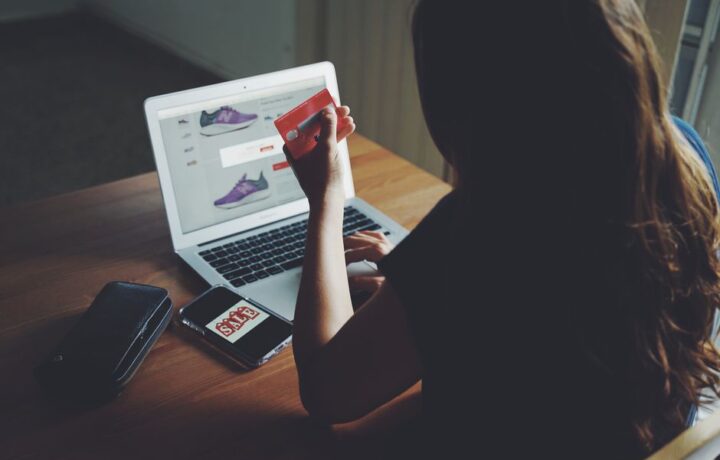 A woman shops online using a laptop and credit card on a wooden table.