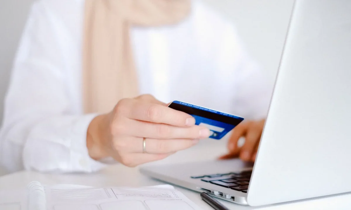 Close-up de uma pessoa segurando um cartão de crédito enquanto usa um laptop para compras online