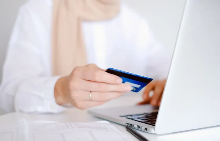 Close-up de uma pessoa segurando um cartão de crédito enquanto usa um laptop para compras online