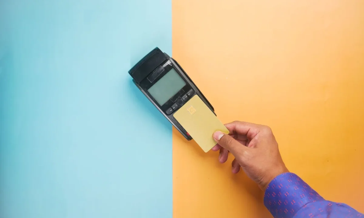 Mão utilizando um cartão de crédito em um terminal de pagamento para transação sem contato, ilustrando erros link de