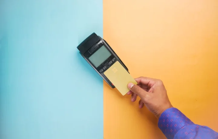 Mão utilizando um cartão de crédito em um terminal de pagamento para transação sem contato, ilustrando erros link de