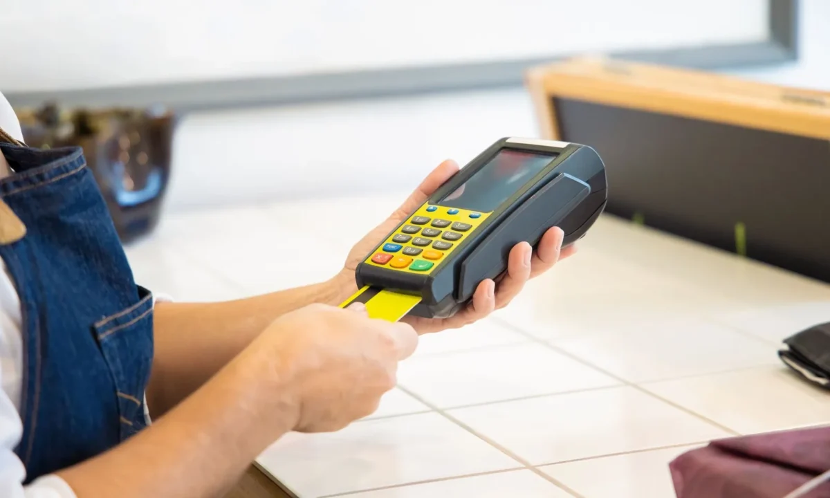 Mãos operando um terminal de pagamento com cartão em um ambiente comercial, ilustrando custo subadquirente e-commerce