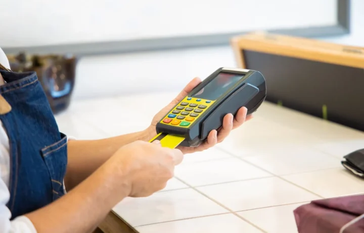 Mãos operando um terminal de pagamento com cartão em um ambiente comercial, ilustrando custo subadquirente e-commerce