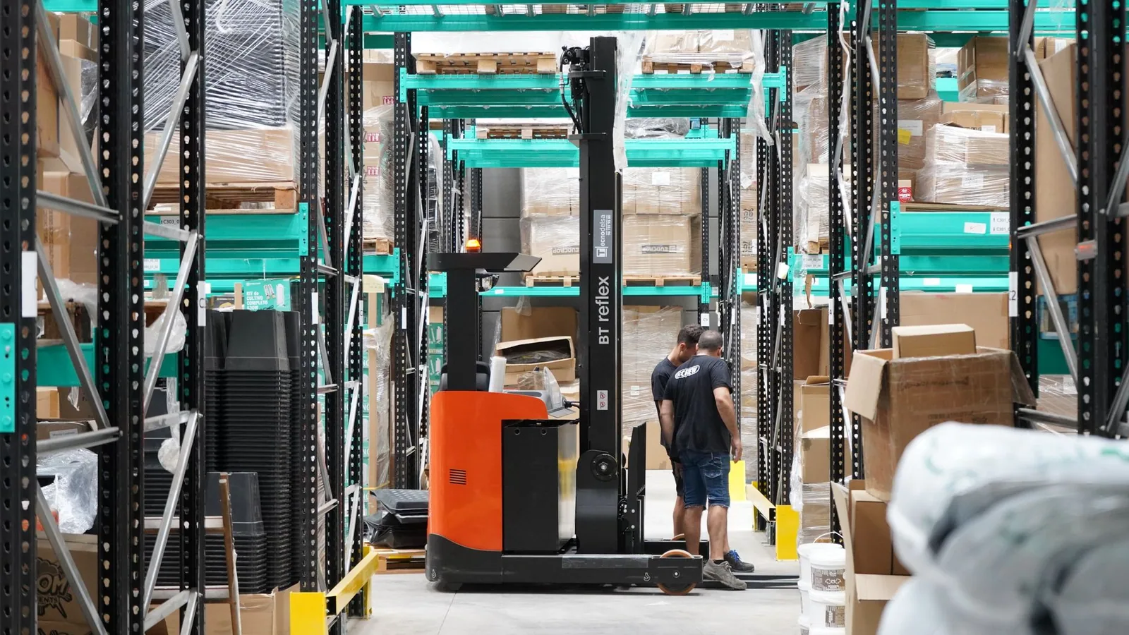 Trabalhadores e um empilhadeira em ação em um armazém, destacando a otimização de rotas de entrega com IA